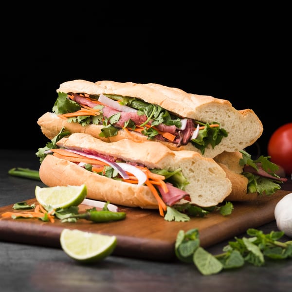 Two banh mi sandwiches with meat, cilantro, and pickled vegetables on a wooden board.