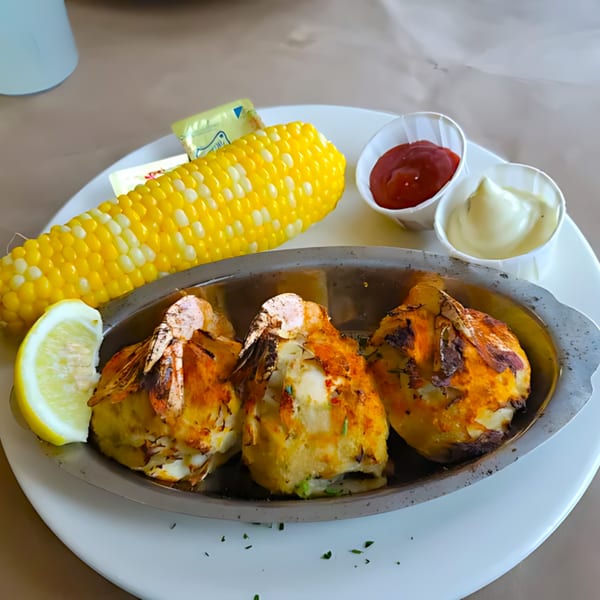 Three baked stuffed clams with a lemon wedge, corn on the cob, ketchup, and mayonnaise.