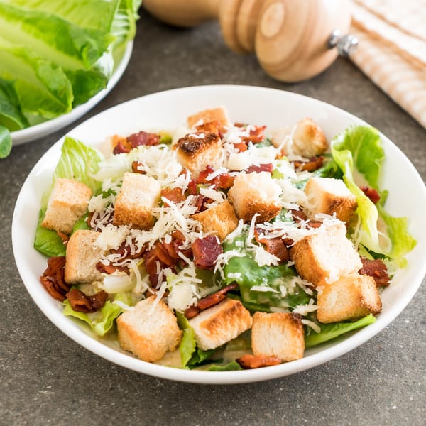 A Caesar salad with romaine lettuce, croutons, bacon bits, and shredded Parmesan cheese.