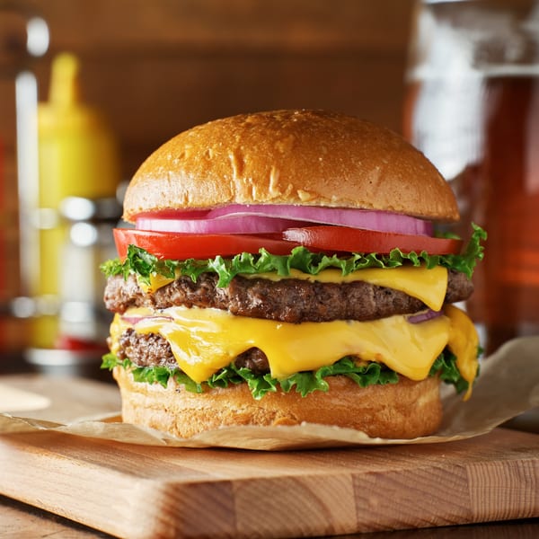 A double cheeseburger with lettuce, tomato, and red onion on a wooden board at Meadowlands Diner.