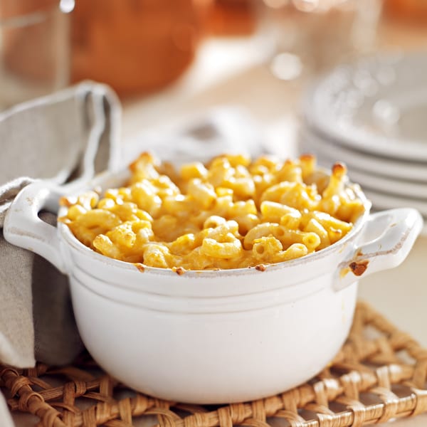 A white ceramic bowl filled with golden-brown baked macaroni and cheese, on a woven placemat.